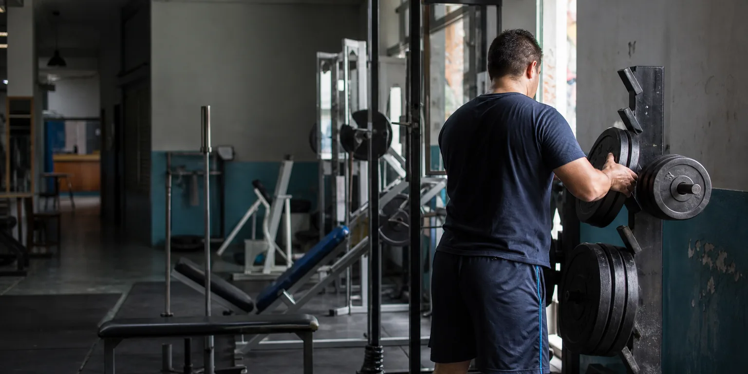 Sala de musculación de barrio con una persona acomodando discos en un rack